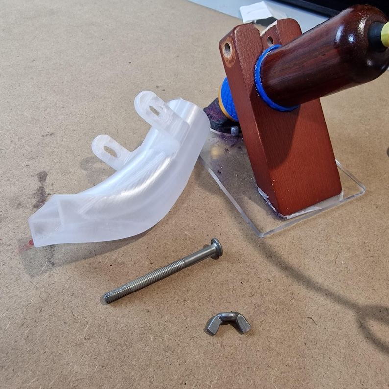 May include: A disassembled wooden stamp with a clear plastic base, a clear plastic curved piece, a bolt, and a wing nut. The stamp has a dark brown handle and a blue ring.