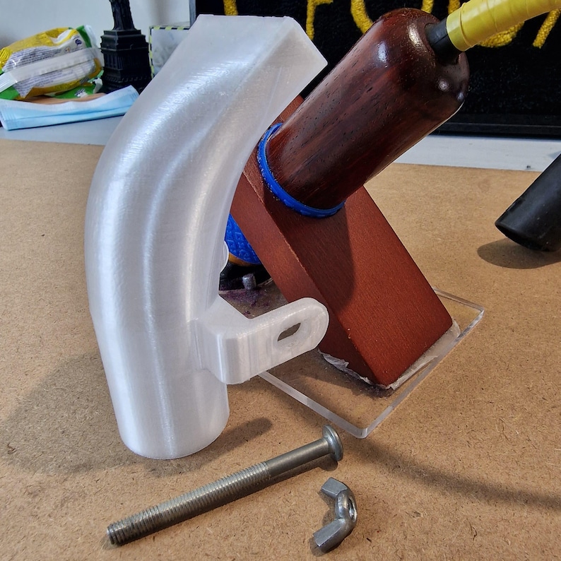 May include: A white, curved 3D-printed part with a mounting tab, alongside a wooden component with a dark finish and a bolt with a wing nut. The wooden piece is mounted on a clear acrylic base.