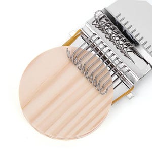 Puede incluir: Un llavero de madera con una base circular marrón claro y una serie de ganchos plateados. El llavero tiene una parte superior de acero inoxidable con anillos adicionales. Una banda elástica amarilla asegura la base de madera al marco de metal.