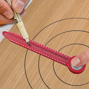 Puede incluir: Una herramienta de corte circular roja con medidas en centímetros se utiliza para dibujar un círculo sobre una superficie de madera. La herramienta tiene un cuerpo rojo con una escala de medición y se utiliza un bolígrafo para dibujar el círculo.