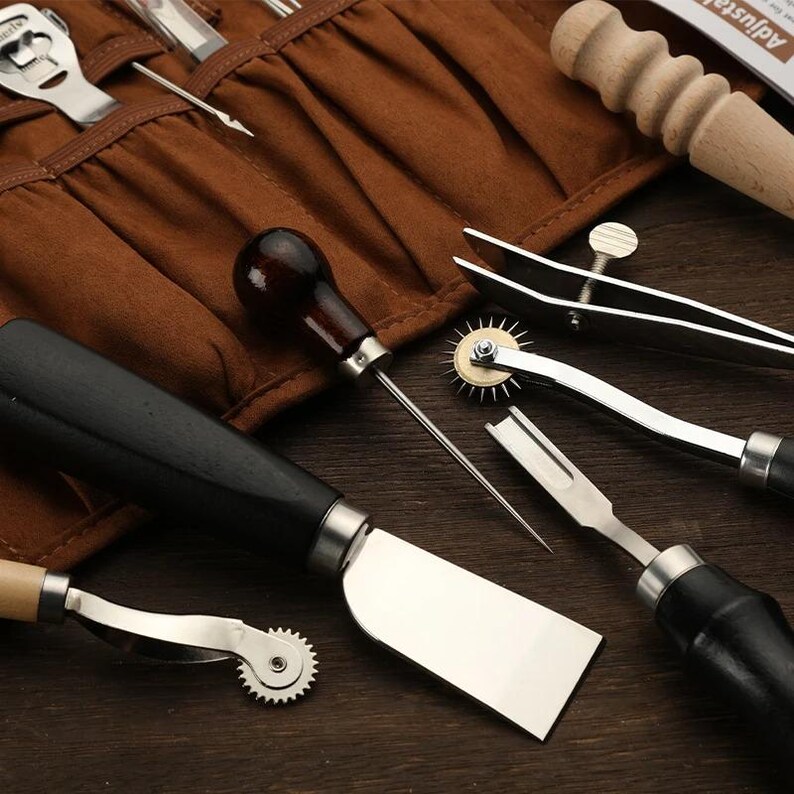 May include: A collection of leatherworking tools, including a burnisher, edge creaser, stitching groover, and various other instruments. The tools have wooden handles and stainless steel blades, arranged on a brown leather tool roll.