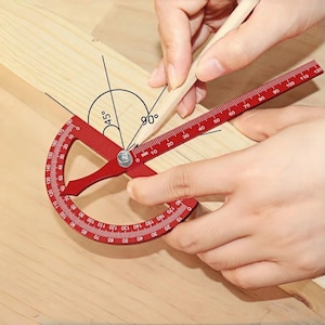 May include: A red protractor tool with a ruler and a curved scale is used to measure angles on a piece of wood. The tool is marked with numbers and degree measurements. The image shows a 45-degree angle and a 90-degree angle.