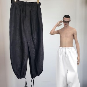 Può includere: Pantaloni neri ampi con vita con coulisse e lacci alle caviglie appesi a un'appendiabiti. Una persona indossa pantaloni bianchi ampi con vita con coulisse e lacci alle caviglie. I pantaloni hanno una forma voluminosa unica.