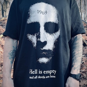 Puede incluir: Camiseta negra con un gráfico blanco desgastado de una cara y el año "1969" encima. Debajo, el texto dice "Hell is empty and all devils are here".