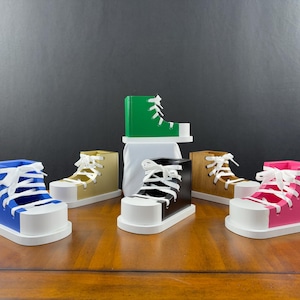 May include: A display of high-top sneaker-shaped boxes in a range of colours. The boxes, with white soles and laces, are in blue, green, black, pink, and tan. They are arranged on a wooden surface.