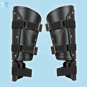 May include: Pair of black leather arm guards with riveted accents and adjustable black straps with silver buckles. The arm guards are designed to protect the forearms and are likely for costume or historical reenactment purposes.