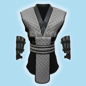 May include: A gray and black quilted costume with matching arm guards. The costume features a V-neck design and a quilted pattern on the chest and lower portion. The arm guards are black with adjustable straps. The text "Mythical Made Designs" is visible.