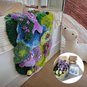 Peut inclure: Un tapis textur&eacute; et color&eacute; avec un motif de paysage dans des tons de vert, violet, bleu et jaune. Le tapis est pos&eacute; sur un lit. Un ours polaire en peluche et un panier de laine sont &eacute;galement pr&eacute;sents.