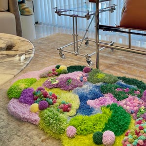 Peut inclure: Un tapis abstrait color&eacute; avec une vari&eacute;t&eacute; de textures et de couleurs. Le tapis pr&eacute;sente un m&eacute;lange de teintes vertes, bleues, violettes et roses, avec un aspect duveteux et textur&eacute;. Le design comprend des pompons et des sections touffues, cr&eacute;ant un rev&ecirc;tement de sol artistique unique.