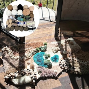 May include: A handcrafted rug with a landscape design featuring blue, green, and beige textures. The rug is decorated with tufted elements and pom-poms. A collection of yarn balls in various colours is also present.