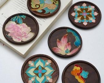 May include: Six round wooden coasters with detailed floral and cloud patterns. Each coaster has a unique hand-painted design in pink, blue, green, and yellow, set against a dark wood background. The coasters are displayed on a book.