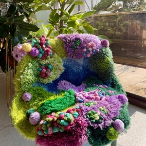 Peut inclure: Une chaise fantaisiste avec un design color&eacute; et textur&eacute;. L'assise pr&eacute;sente un m&eacute;lange vibrant de vert, bleu, violet et rose, avec une vari&eacute;t&eacute; de textures et de pompons. Les pieds de la chaise sont vert p&acirc;le.