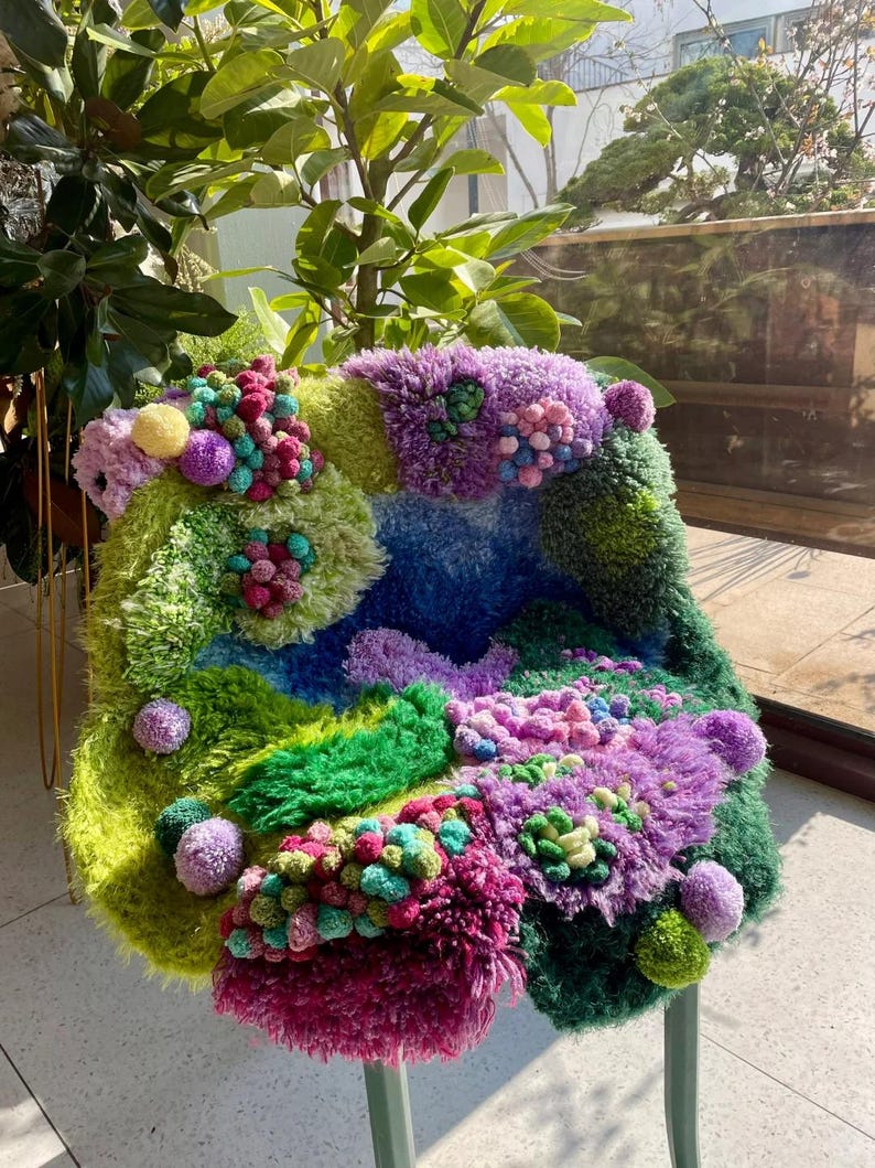 Peut inclure: Une chaise fantaisiste avec un design color&eacute; et textur&eacute;. L'assise pr&eacute;sente un m&eacute;lange vibrant de vert, bleu, violet et rose, avec une vari&eacute;t&eacute; de textures et de pompons. Les pieds de la chaise sont vert p&acirc;le.