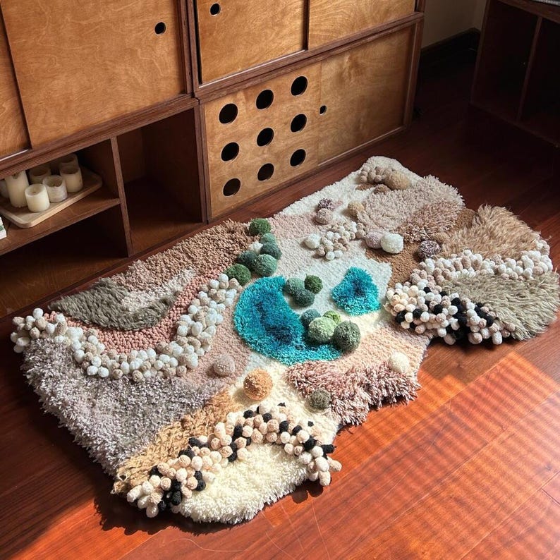 以下が含まれることがあります： ユニークな抽象デザインの手作りのテクスチャードラグ。 ターコイズ、グリーン、ベージュ、ブラウンなど、さまざまな色とテクスチャが特徴です。 隆起した房状の要素と柔らかく豪華な感触で、風景のような外観をしています。 木の床に置かれたラグです。