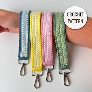 May include: Four crochet wristlet lanyards in light blue, yellow, pink, and sage green, each featuring a silver-toned metal lobster clasp at the bottom. A circular white graphic overlay in the upper right corner displays the text CROCHET PATTERN.