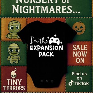 May include: Black baby bodysuit with the text "I'm the EXPANSION PACK" and a controller graphic. The bodysuit is centered on a patchwork background with Halloween-themed graphics and the phrase "WELCOME TO THE NURSERY of NIGHTMARES..."