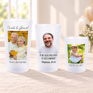 Könnte beinhalten: Drei mattierte Kunststoffbecher in verschiedenen Größen, jeweils mit individuellem Foto und Text. Der größte Becher zeigt ein Paar mit dem Text 'Carole & Gérard 50 ans de mariage'. Der mittlere Becher zeigt einen Mann mit 'JE NE SUIS PAS VIEUX, JE SUIS VINTAGE! Stéphane, 51 ans'. Der kleinste Becher zeigt ein Kind mit 'LENA FÊTE SES 6 ANS!'