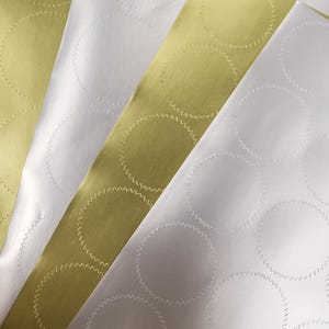 Peut inclure: Plusieurs feuilles d'étiquettes adhésives en or métallique et blanc mat disposées en éventail superposé. Chaque feuille présente une grille d'autocollants circulaires avec des bords dentelés en zigzag distincts gaufrés sur la surface.