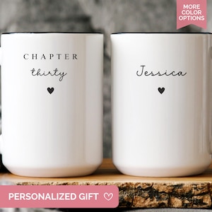May include: Two white ceramic mugs with black handles and rims. One mug reads "CHAPTER thirty" with a heart, the other says "Jessica" with a heart. The mugs are on a wooden surface. Text at the bottom reads "PERSONALIZED GIFT".