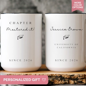May include: Two white ceramic mugs with black handles and rims. One mug reads "CHAPTER Mastered it!" and the other "Jessica Brown, University of California." Both mugs have "SINCE 2026" printed at the bottom. A graduation cap graphic is also present.