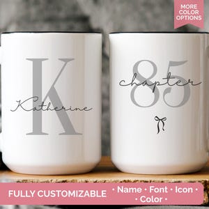 May include: Two white ceramic mugs with black handles and rims. One mug features a gray letter "K" and the name "Katherine" in script. The other mug displays the number "85" and the word "chapter" in script, with a small bow icon. The mugs are fully customizable.