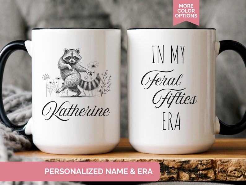 White ceramic mug featuring a hand-drawn raccoon holding a flower on one side with personalized name, and the phrase “In My Feral Fifties Era” on the other.