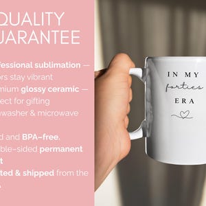 May include: White ceramic mug with the text "IN MY forties ERA" in black script and a heart symbol. The mug has a white handle and is held by a person. The image also includes text about the product's quality.