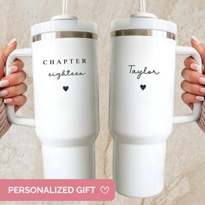 May include: Two white insulated tumblers with handles. One tumbler has the text "CHAPTER eighteen" and a heart. The other has the name "Taylor" and a heart. Both tumblers have a white lid and a silver band.