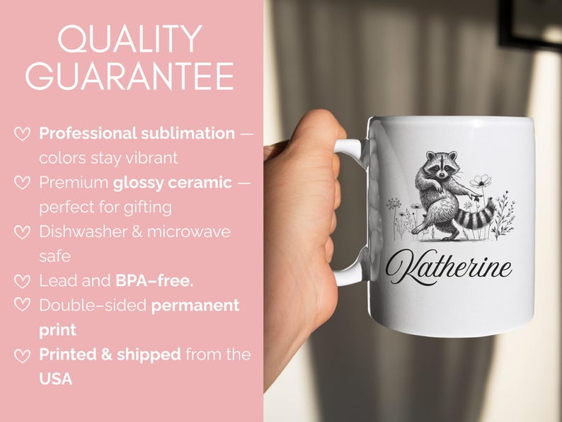 May include: White ceramic mug featuring a black and white illustration of a raccoon with a flower and the name "Katherine" in cursive. The mug has a white handle and is held by a person.