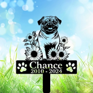 May include: Black metal garden stake featuring a pug dog design with sunflowers. The stake includes the name "Chance" and the years "2010 - 2024" with paw prints on either side. The background is a blurred image of grass and sky.