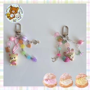 以下が含まれることがあります： 漫画のクマのチャーム、カラフルなビーズ、音符のチャームが付いた2つのキーホルダー。1つのキーホルダーには星型のビーズストランドが付いています。もう1つはイチゴのチャームが付いています。下部には、さまざまなフィリングが入った3つのシュークリームがあります。