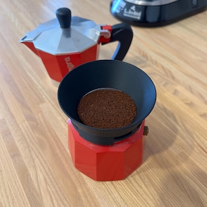 Peut inclure: Une tasse en céramique blanche avec une anse noire et le texte "But First, Coffee" en noir, dans une police manuscrite. La tasse est posée sur une surface blanche.