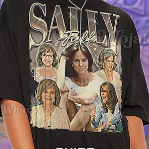May include: Black unisex t-shirt featuring a graphic of Sally Field with the text "SALLY Field". The shirt has a vintage style design. The text "SHIRT Unisex" is printed at the bottom.