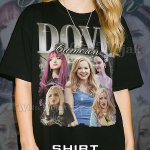 May include: Black unisex t-shirt featuring a graphic of Dove Cameron with the text "DOVE Cameron" in silver. The shirt also has the text "SHIRT Unisex" in white. The model is wearing a 2XL shirt.