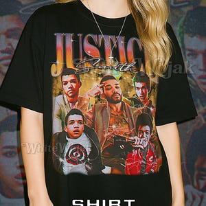 May include: Black unisex t-shirt featuring a graphic of a group of men with the text "JUSTICE Smith". The shirt also has the word "SHIRT" above "Unisex" in a cursive font. The model is wearing a 2XL shirt.