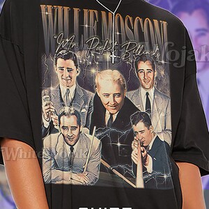 May include: Black unisex t-shirt featuring a vintage-style graphic of Willie Mosconi, a famous billiards player, with text that reads "Willie Mosconi" and "Mr. Pocket Billiards." The shirt also has the word "Unisex" printed on it.