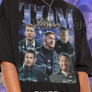 May include: Black unisex t-shirt featuring a graphic of several men with the text "TOM Hopper Wojak". The shirt also has the text "SHIRT Unisex". The first model is wearing a 2XL unisex shirt.