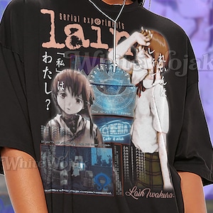 May include: Black unisex t-shirt featuring a graphic design with the text "serial experiments lain" and Japanese text. The design includes anime-style illustrations of a girl and other graphic elements. The shirt also has the text "SHIRT Unisex".