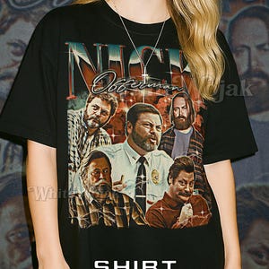 May include: Black unisex t-shirt with a graphic of a group of men and the text "Nick Offerman". The shirt also has the text "Shirt Unisex". The model is wearing a 2XL unisex shirt.