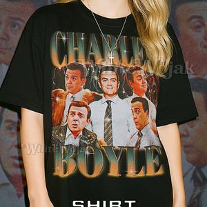 以下が含まれることがあります： 男性グループのレトロなグラフィックと「CHARLIE BOYLE」の文字がプリントされた黒のユニセックスTシャツ。「SHIRT」と「Unisex」の文字もプリントされています。