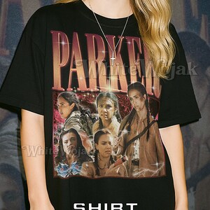 Puede incluir: Camiseta unisex negra con la palabra "PARKER" en una fuente desgastada y un gráfico de mujeres. La camiseta también tiene las palabras "SHIRT Unisex" impresas.
