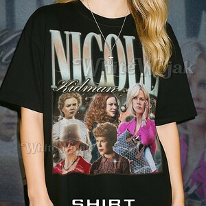 May include: Black unisex t-shirt featuring a graphic of Nicole Kidman with the text "NICOLE KIDMAN". The shirt also has the text "SHIRT Unisex". The model is wearing a 2XL shirt. The shirt fits true to size.
