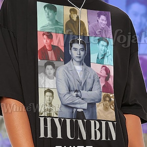 Puede incluir: Camiseta unisex negra con un collage de imágenes de Hyun Bin. La camiseta tiene el nombre "HYUNBIN" impreso en letras blancas grandes, con "SHIRT Unisex" debajo. La camiseta está hecha de un material suave.