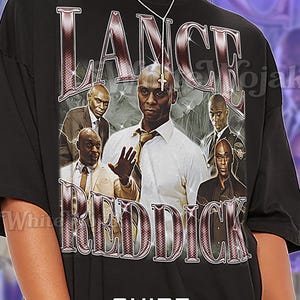 May include: Black unisex t-shirt featuring a graphic of Lance Reddick with the text "LANCE REDDICK". The shirt includes a photo collage of the actor. The shirt also has the text "SHIRT Unisex".