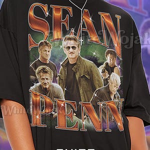 Op de afbeelding: Zwart unisex T-shirt met een afbeelding van Sean Penn en zijn naam in grote, oranje, sprankelende letters. Het shirt heeft het woord "Unisex" onder de afbeelding gedrukt. De tekst op het shirt luidt: "SEAN PENN SHIRT Unisex".
