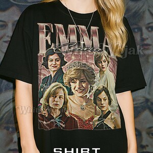 May include: Black unisex t-shirt featuring a graphic of Emma Corrin and other actors. The shirt has the text "EMMA" and "SHIRT Unisex" printed on it. The model is wearing a 2XL shirt.
