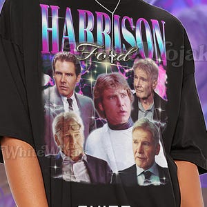 May include: Black unisex t-shirt featuring a graphic of Harrison Ford with the text "HARRISON Ford". The shirt has a vintage style design with a purple and blue color scheme. The shirt is oversized.
