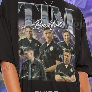 May include: Black unisex t-shirt featuring a graphic design with the name "TIM Bradford" and images of a man in a police uniform. The shirt has the text "SHIRT Unisex" at the bottom.