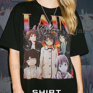 Puede incluir: Camiseta unisex negra con un gráfico colorido de personajes de anime y el texto "Lain". La camiseta también tiene el texto "SHIRT Unisex" en la parte inferior. La modelo lleva una camiseta 2XL.