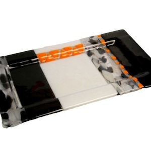 Puede incluir: Una bandeja rectangular de servir de vidrio con un diseño geométrico en blanco y negro. La bandeja tiene un centro blanco con bordes negros y acentos naranjas.